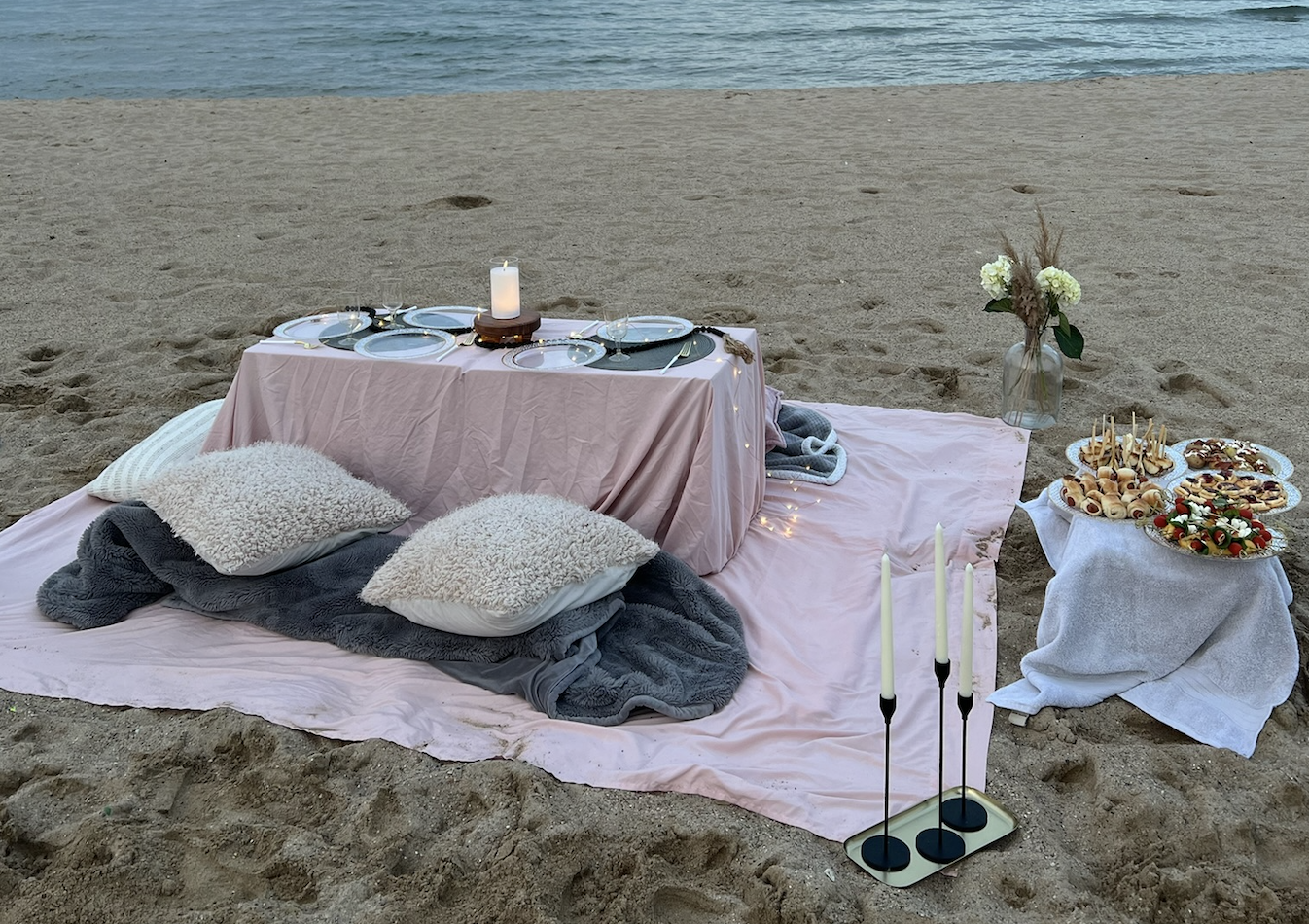 Beachside dinner event with styled table, blankets, candles, and catering